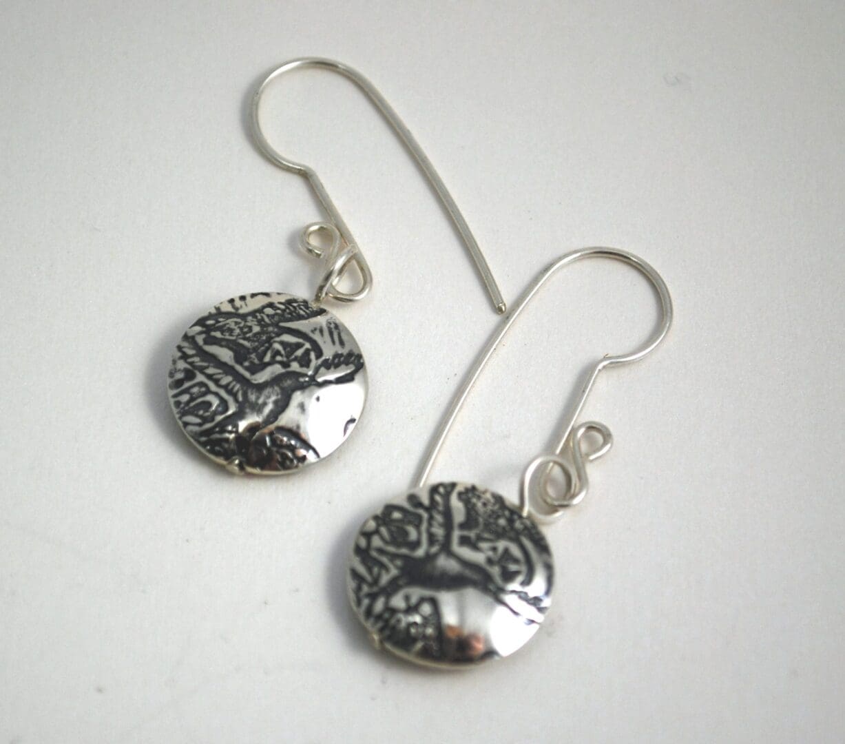 round silver crow earrings with a crow motif embossed on either side of the lentil shaped bead dropper.