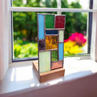 Handmade stained glass candle holder with colourful glass panels in a wooden base, displayed on a sunny windowsill