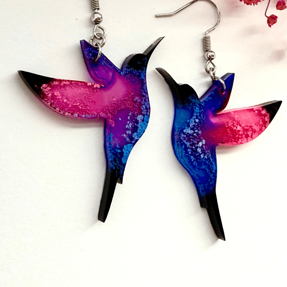 Close-up of handmade pink and blue hummingbird earrings crafted from epoxy resin with alcohol ink effect