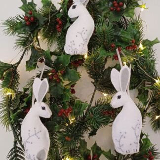 Three Arctic Hare Christmas tree hanging decorations in white felt with embroidered leaves and stems by lyndawilcansew on a winter foliage garland with fairy lights.