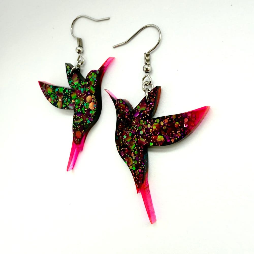 Pair of glitter resin hummingbird earrings under bright light showing sparkle