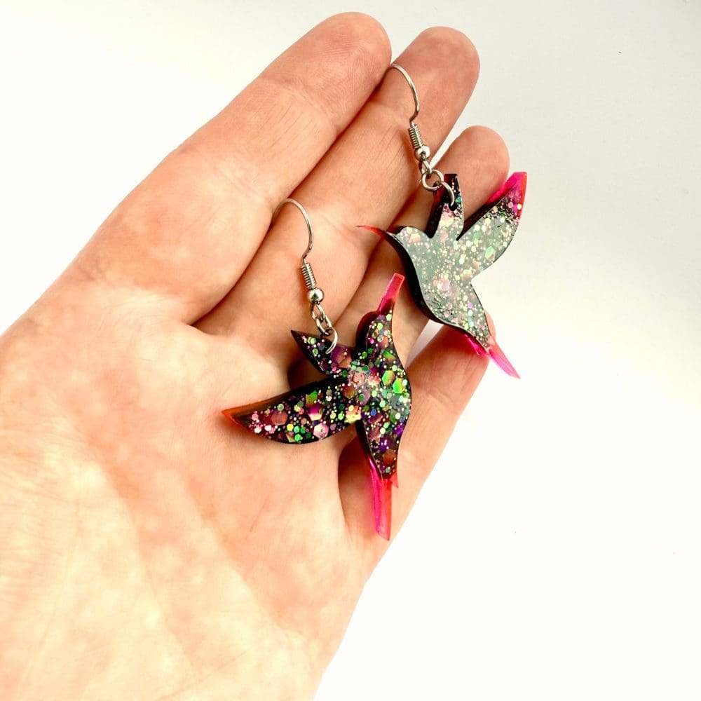 Close-up of dark glitter hummingbird resin earrings on hand to show size