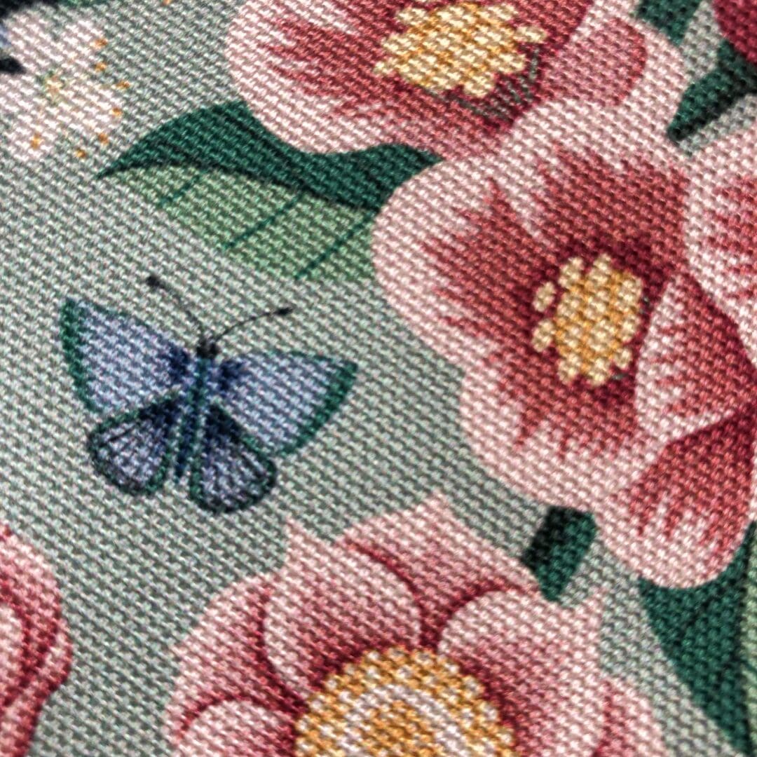 Macro close-up of chinoiserie floral fabric showing intricate hand-painted flowers and butterflies printed in vivid detail.