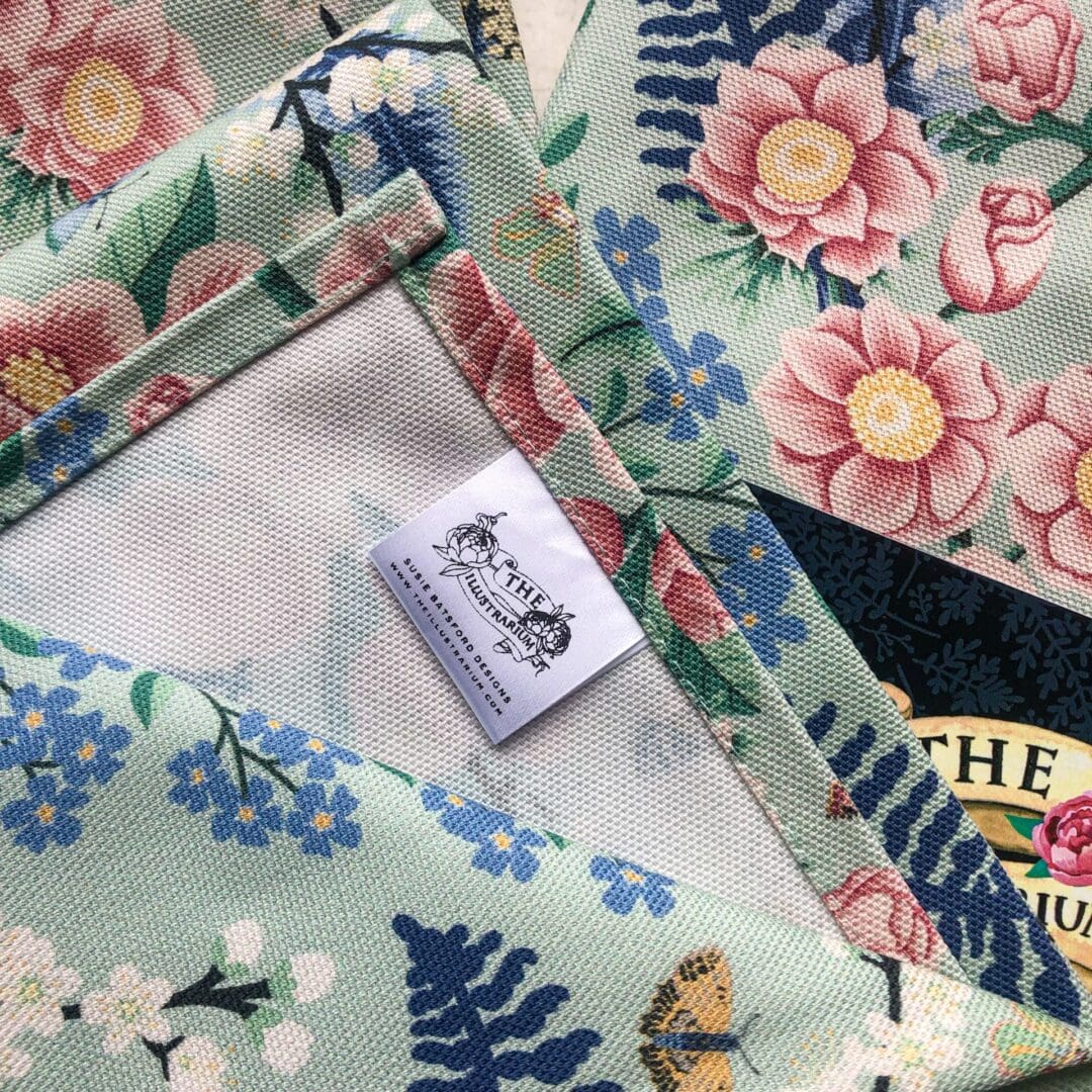 Close-up of folded chinoiserie tea towels showing The Illustrarium woven label and soft cotton texture.