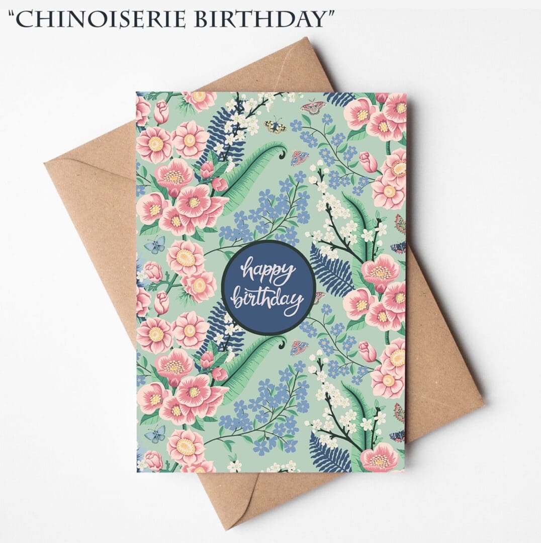 A hand-illustrated birthday card featuring soft blue, pink, and green Chinoiserie-style flowers with the words “Happy Birthday,” displayed on a natural brown Kraft envelope.