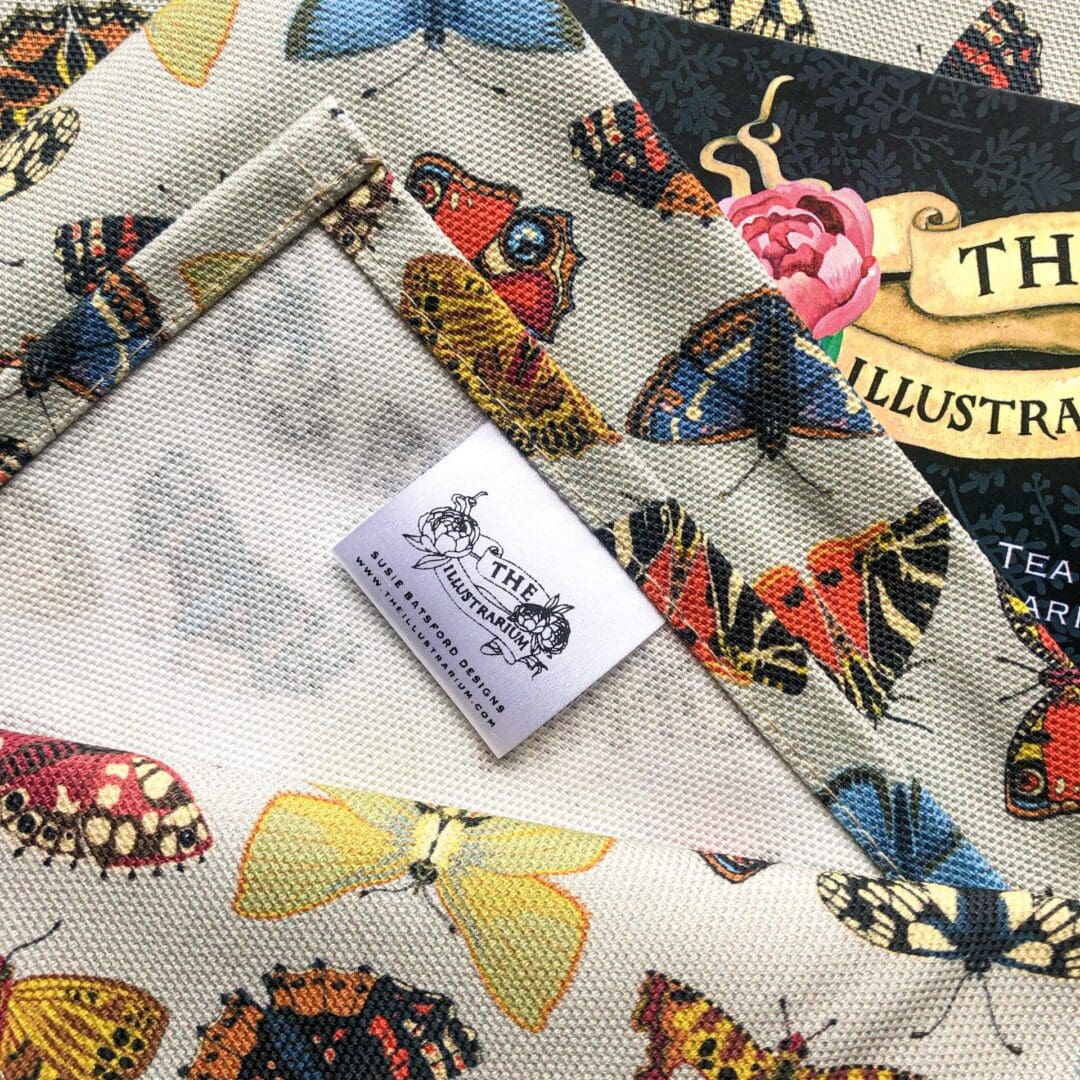 Close-up of the sewn label on the Folk Butterflies Tea Towel, showing The Illustrarium logo and fine hem detail.