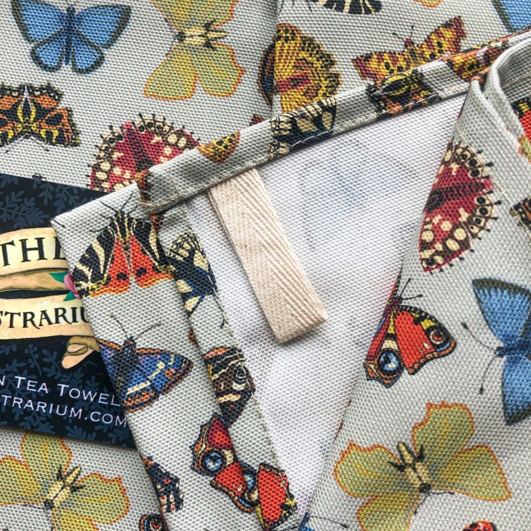 Close-up of the cotton hanging loop sewn into the corner of the Folk Butterflies Tea Towel, surrounded by colourful butterfly illustrations.