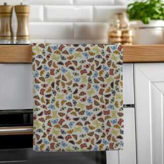 A colourful cotton tea towel featuring hand-illustrated butterflies in folk art style, hanging neatly on a wooden oven rail in a bright modern kitchen.