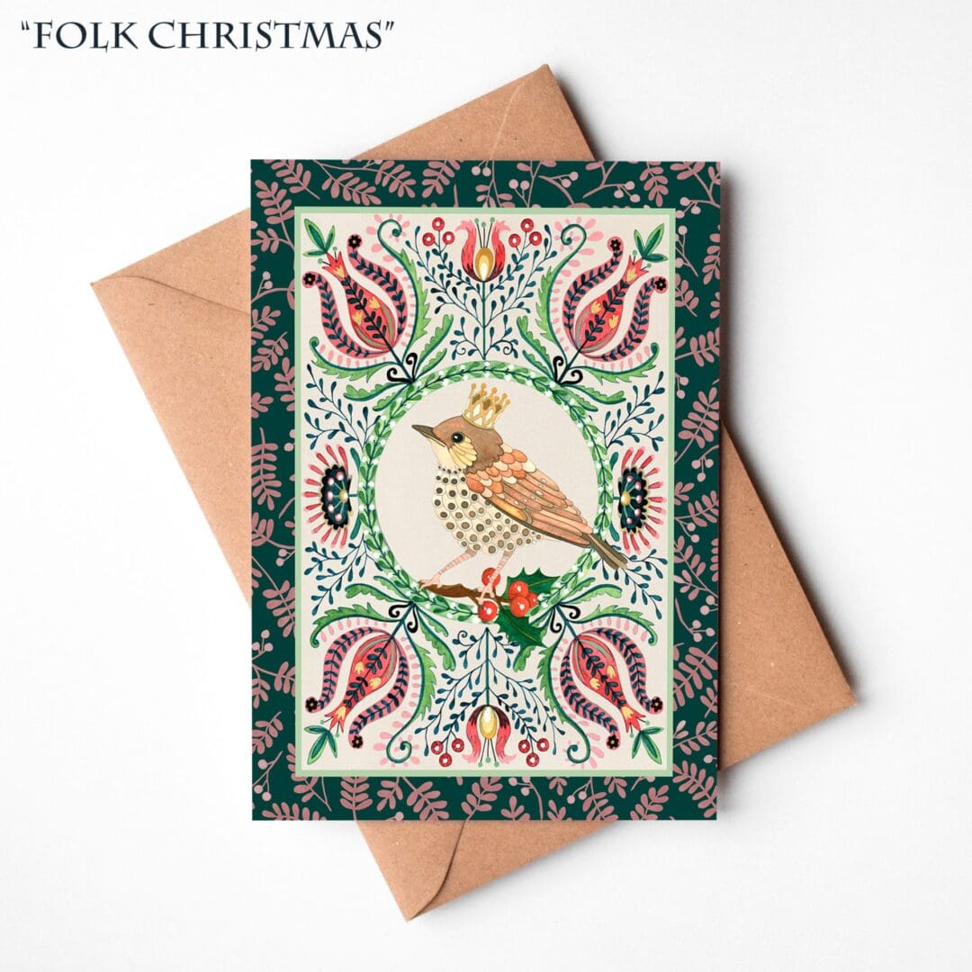 A hand-illustrated Christmas card featuring a crowned robin surrounded by festive greenery and berries, resting on a natural brown Kraft envelope.
