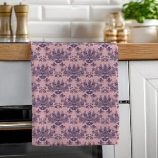 A pink cotton tea towel featuring blue hand-drawn orchids and butterflies hanging neatly on a wooden oven rail in a bright kitchen.