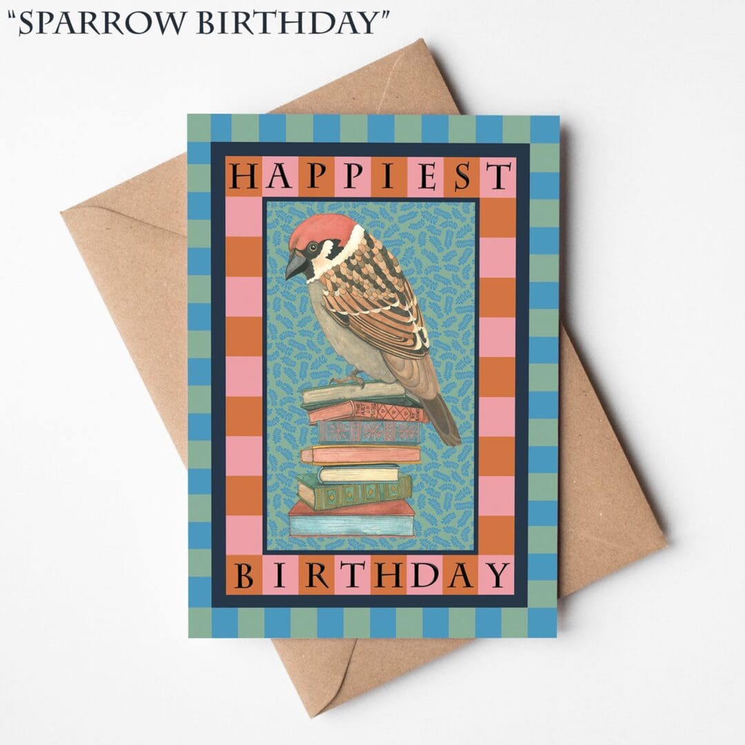 A hand-illustrated birthday card featuring a sparrow perched on a stack of books with the words “Happiest Birthday,” resting on a natural brown Kraft envelope.