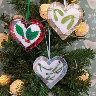Tartan fabric hearts with holly mistletoe and fir branch motifs by lyndawilcansew hung on a green tree with rattan ball fairy lights