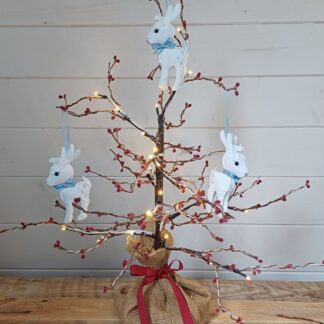 White felt reindeer with silver star motifs by lyndawilcansew hanging on a twig tree against a rustic background