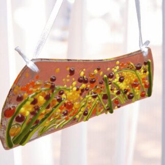 Handmade fused glass suncatcher inspired by autumn meadows, featuring rich amber, green and golden tones. Textured glass catches the sunlight beautifully, creating warm reflections. Measuring 12 cm long, 5 cm at the widest, and hanging 14 cm from a white ribbon, this piece is gift-wrapped in white tissue paper with a purple ribbon. Perfect as a handmade gift or autumn home decoration, lovingly made in my home studio by Sandgate Glass.