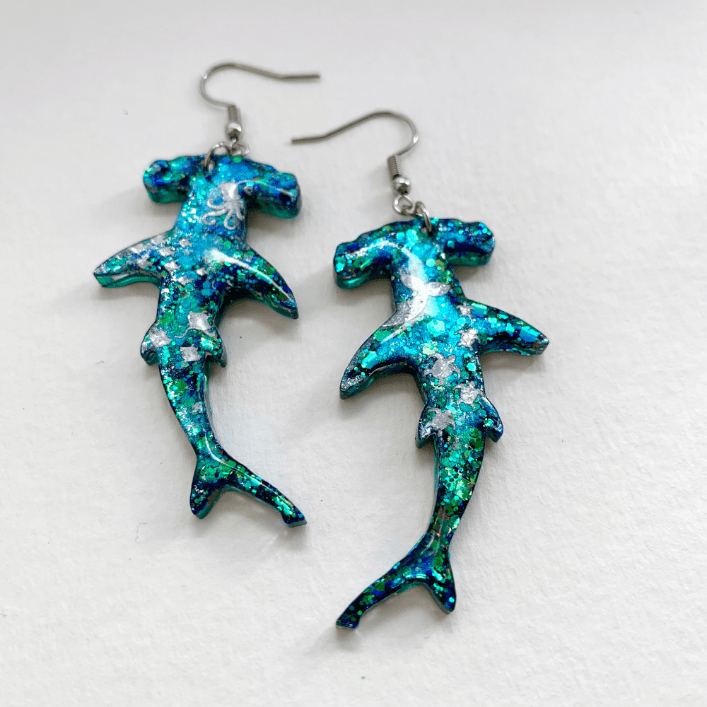 Tilted image of the blue glitter shark earrings showing the almost etheral blue glow.