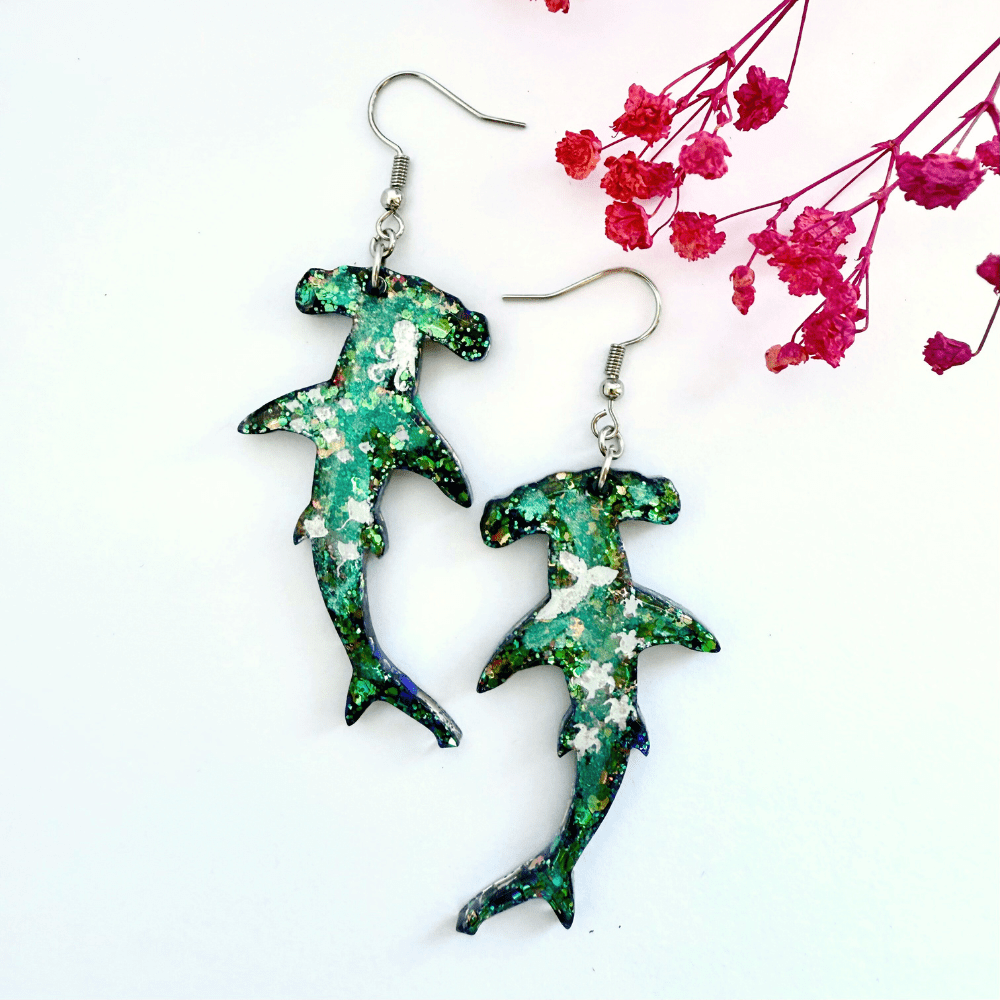 Beautiful shimmering glitter hammerhead sharks with marine life impressions and "salt spray" glitter embellishment on a white background with pink flower decoration.