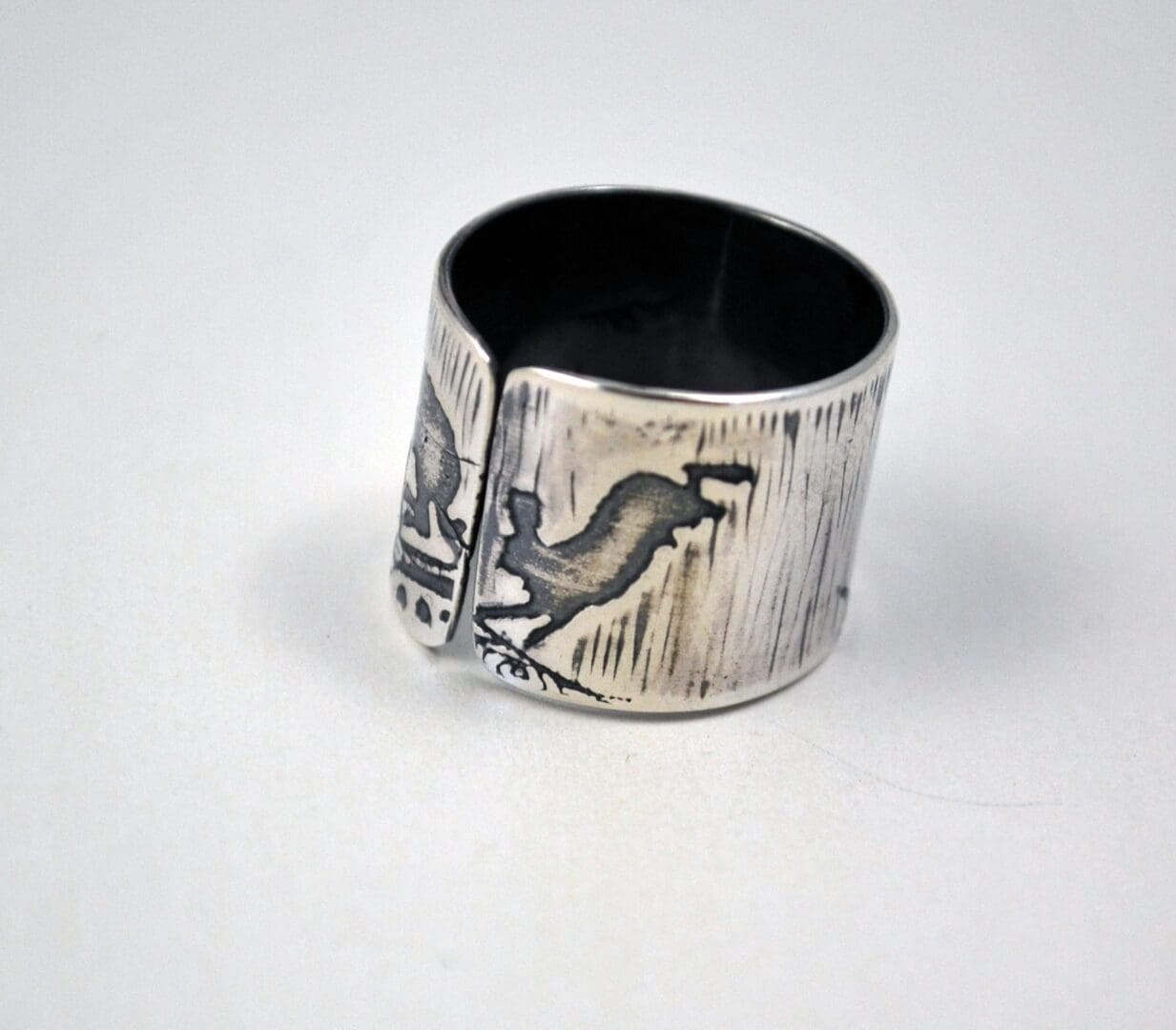 A rear view of a wide, sterling silver cuff ring, featuring a prominent, centrally-placed etched and oxidized design of a leaping hare.