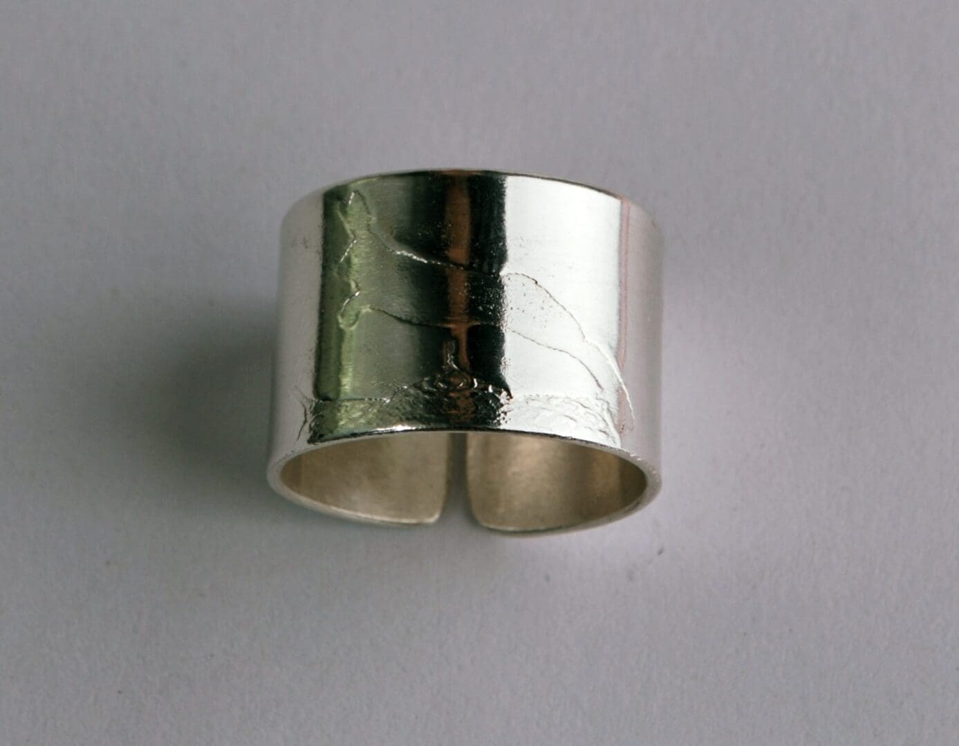 A front-on view of a wide, sterling silver cuff ring with a high-polish, mirror-like finish. A subtle, etched design of a leaping hare is visible, catching the light on the reflective surface. The ring's open gap is visible at the bottom.