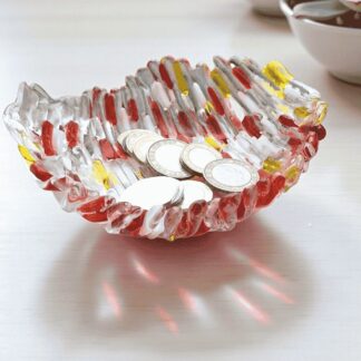 A handmade fused glass trinket dish in red, yellow, and clear glass, designed with a textured ripple pattern. The bowl is shown holding coins, highlighting its use as a decorative storage dish for keys, jewellery, or loose change. Ideal as a unique handmade gift or modern home décor accent, this handcrafted glass art piece reflects light beautifully, adding colour and texture to any tabletop or display.