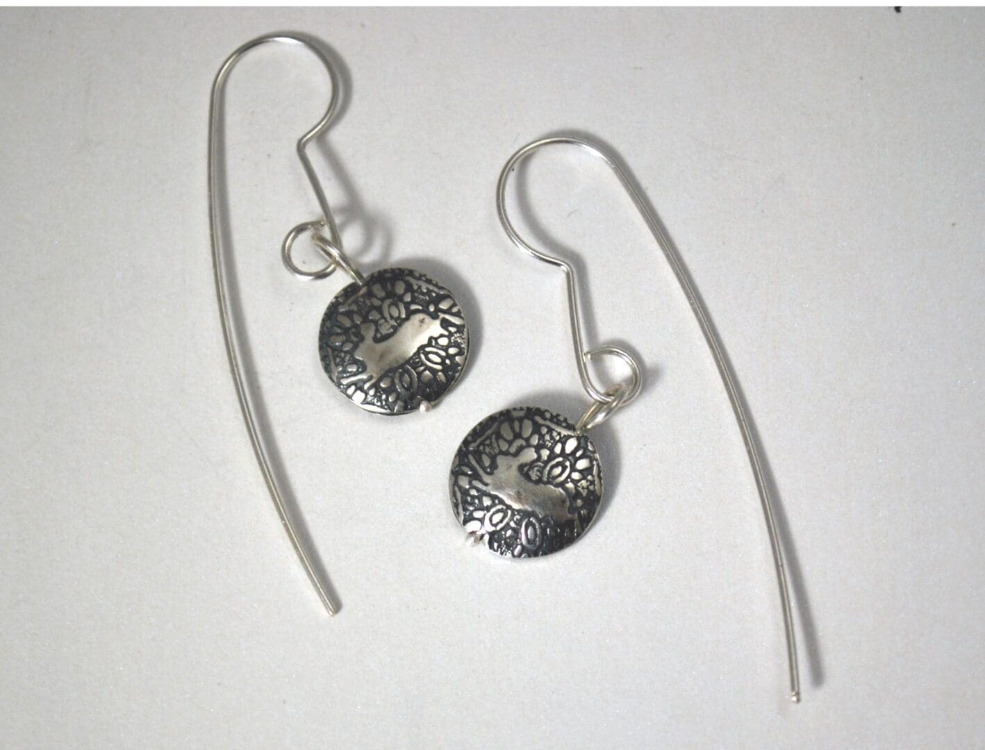 A pair of handmade sterling silver drop earrings with long ear wires. Each round, oxidized silver disc features a textured mandala-like background with a leaping hare silhouette in the center