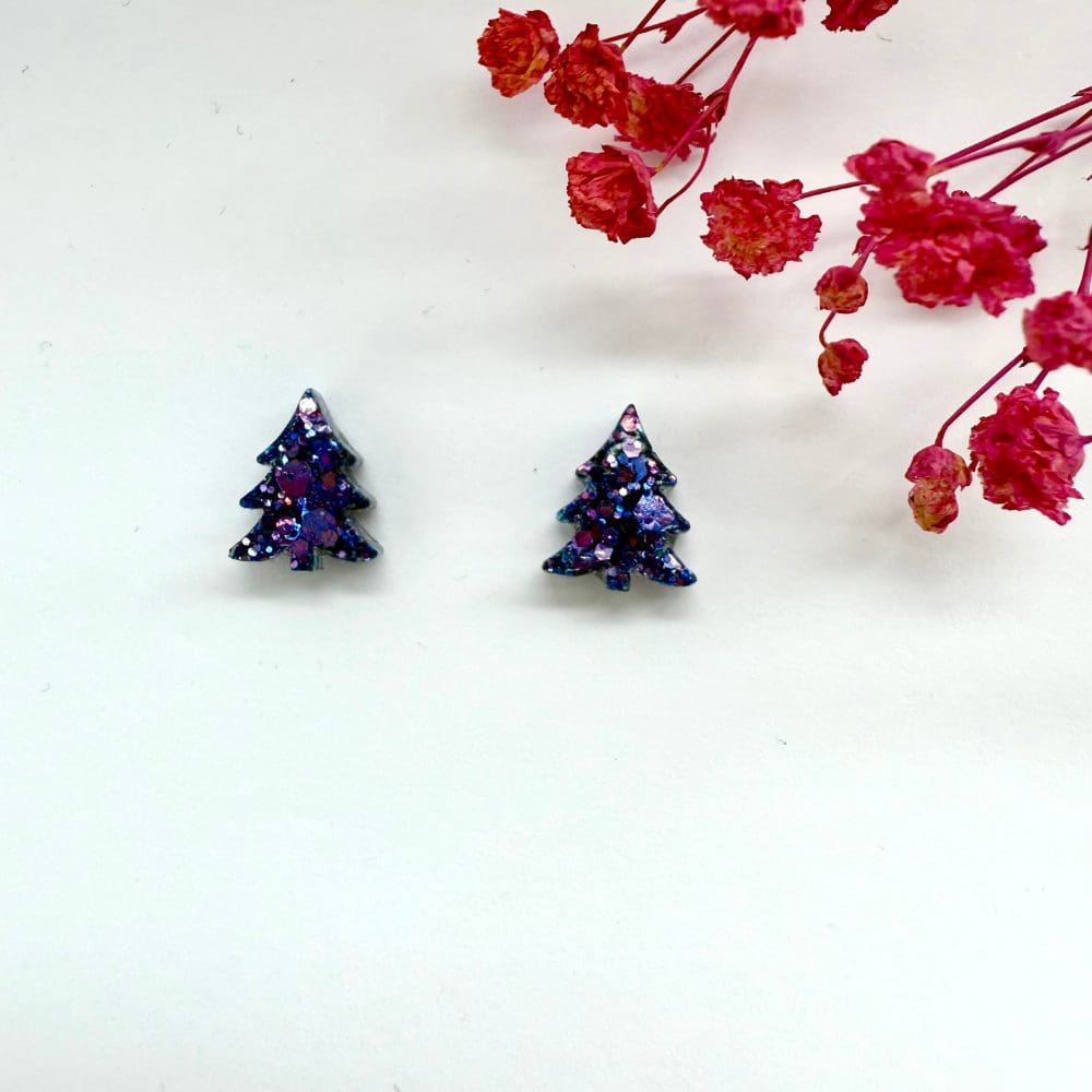 Close-up of purple glitter Christmas tree stud earrings on a white background.