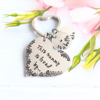 A heart shaped aluminium keyring hand stamped with 'this mummy is loved by' with personalised name discs.