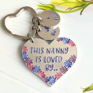aluminium heart keyring hand-stamped with 'this Nanny is loved by' coloured blue with coloured flower details and blue lettered personalised name tags