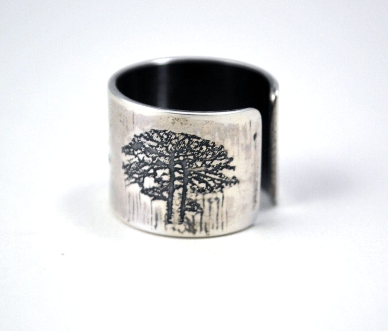 A close-up shot of a textured sterling silver cuff ring with a dark etched tree design, seen from a slightly lower angle than previous views, on a white background