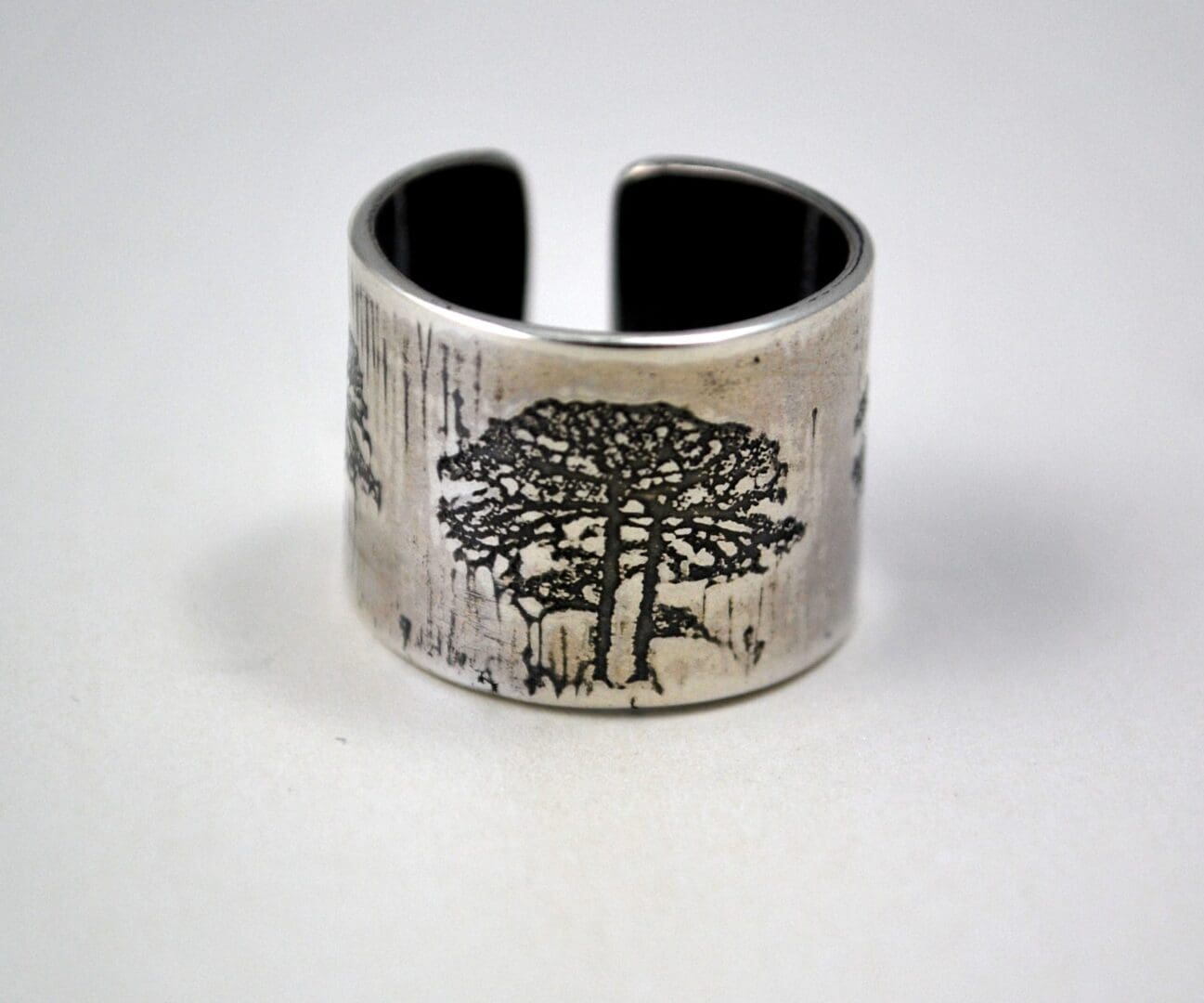 A wide, rustic sterling silver cuff ring with a large, detailed etching of a tree, seen from a high-angle front view that clearly shows the ring's open back