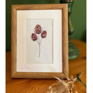A wooden framed artwork featuring a single stem teasel with three brown heads. Created by embroidery.