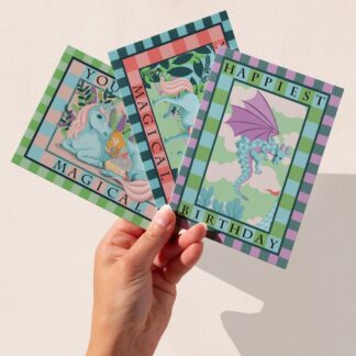 Three fantasy greeting cards featuring unicorn and dragon illustrations in pastel hues by The Illustrarium.