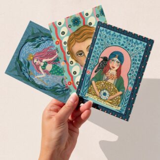 Hand holding three art greeting cards featuring The Illustrarium’s hand-painted Mermaid, Virginia Woolf, and Fortune Teller designs, printed on eco-friendly recycled card.