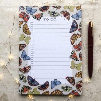 A5 Butterfly & Moth To-Do Notepad featuring colourful hand-painted butterflies and moths on a pale beige background, with a red pen and fairy lights beside it.
