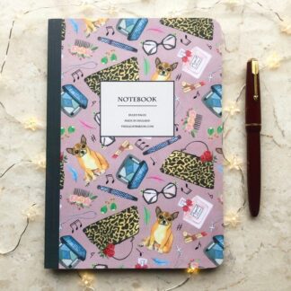 A hand-painted A5 notebook featuring chihuahuas and vintage-style fashion accessories on a pink background, styled with a red fountain pen and delicate fairy lights.