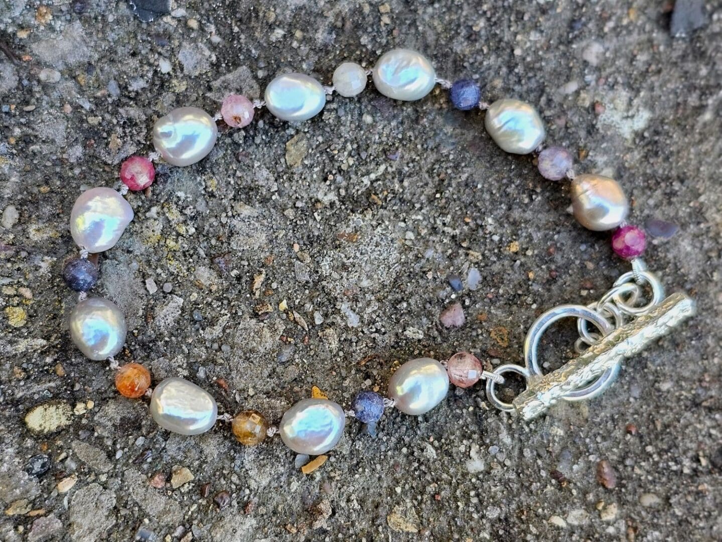 Grey baroque pearl, ruby & sapphire gemstone bead bracelet, outdoor shot on stone, Isobel Kelly Jewellery