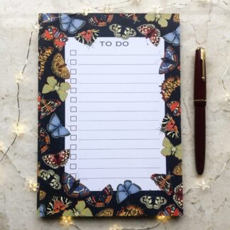 A5 butterfly and moth notepad on marble with fairy lights and red pen, featuring colourful hand-painted insects on a dark background.