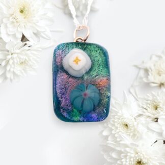 A rectangular glass pendant with a shimmering iridescent surface, featuring a white and blue flower design. Surrounded by white chrysanthemums, conveying elegance.