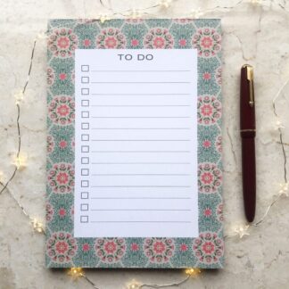 A5 Daisy floral notepad featuring hand-painted pink and green daisy pattern on recycled paper, with a red pen and fairy lights beside it.