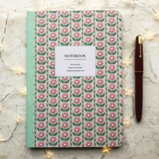 A hand-painted A5 notebook with mint green stripes and white daisy motifs, styled with fairy lights and a vintage red fountain pen on a marble background.