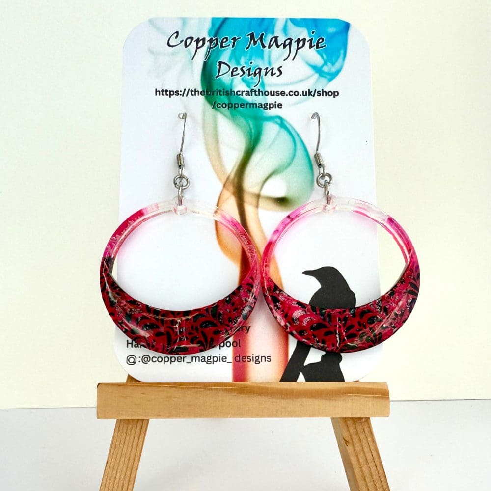 Gothic style round hoop floral lace earrings in pink with black background hanging on hypoallergenic surgical steel earrings hooks. These are displayed on a Copper Magpie Designs branded earrings cards.