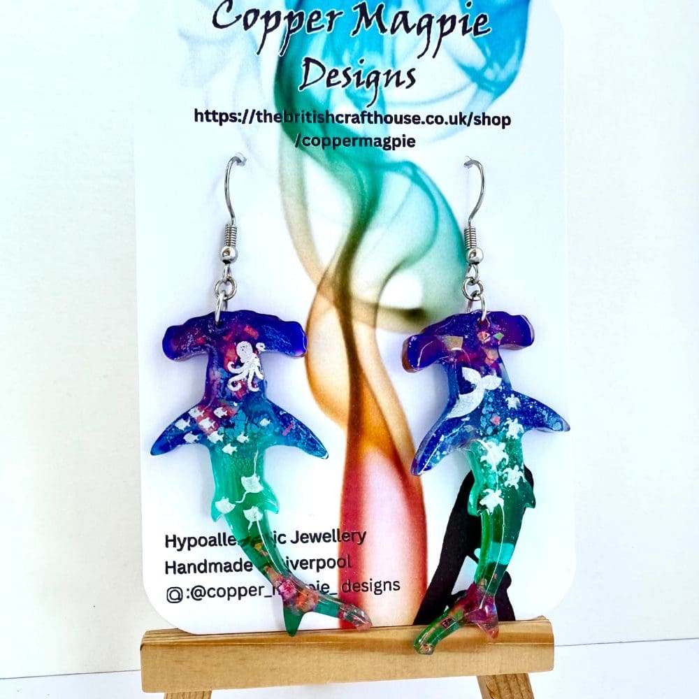 Blue and green hombre hammerhead shark earrings with glitter embelishment, with marine creature patterns. Hung on surgical steel earhooks. Presented on a branded Copper Magpie Designs card.