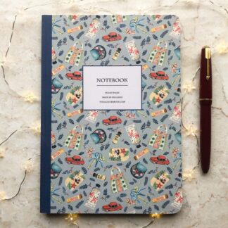 A beautifully illustrated A5 notebook featuring hand-painted fashion and vintage-inspired designs, including handbags, perfume, and flowers, shown with a red pen and warm fairy lights on a marble background.