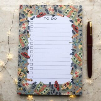 A hand-painted A5 to-do notepad featuring a whimsical design of handbags, vintage accessories, and retro motifs on a soft grey background, styled with fairy lights and a red fountain pen.