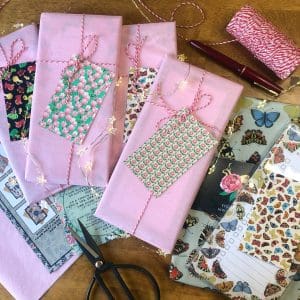 Eco-friendly packaging at The Illustrarium: pink tissue-wrapped parcels with patterned gift tags, twine, and studio tools.