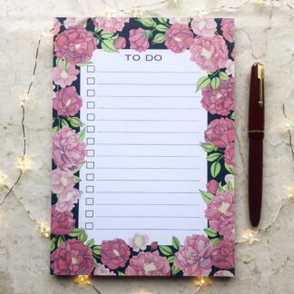 A hand-painted A5 to-do notepad with pink peonies and green leaves on a dark background, styled with a red fountain pen and fairy lights.