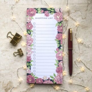Pink peony floral shopping list notepad with hand-painted design, styled with gold clips, fairy lights, and a red pen on a marble background.