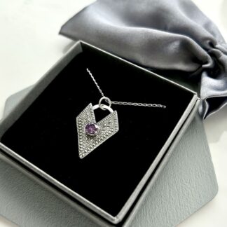 A fine silver handmade pendant that is textured and has a v shape with a 5mm. cubic zirconia amethyst in the centre. It has a sterling silver chain and is displayed in a grey gift box.