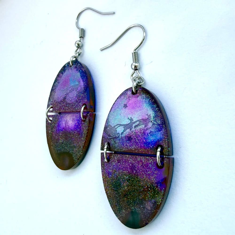 Close-up of holographic northern lights resin earrings with Santa sleigh silhouette and glittery forest scene