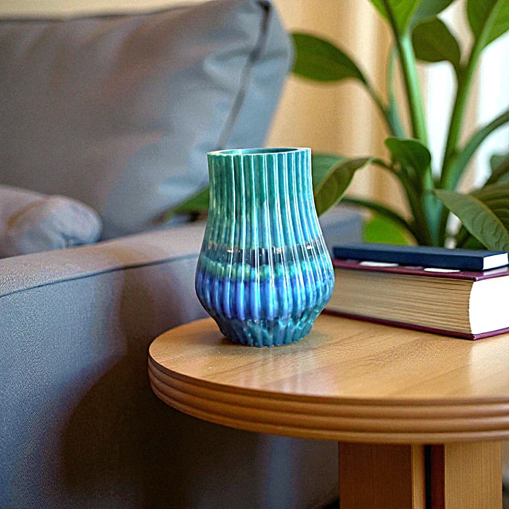 Green and blue striped fluted vase in front of a book on a small wooden table next to a sofa