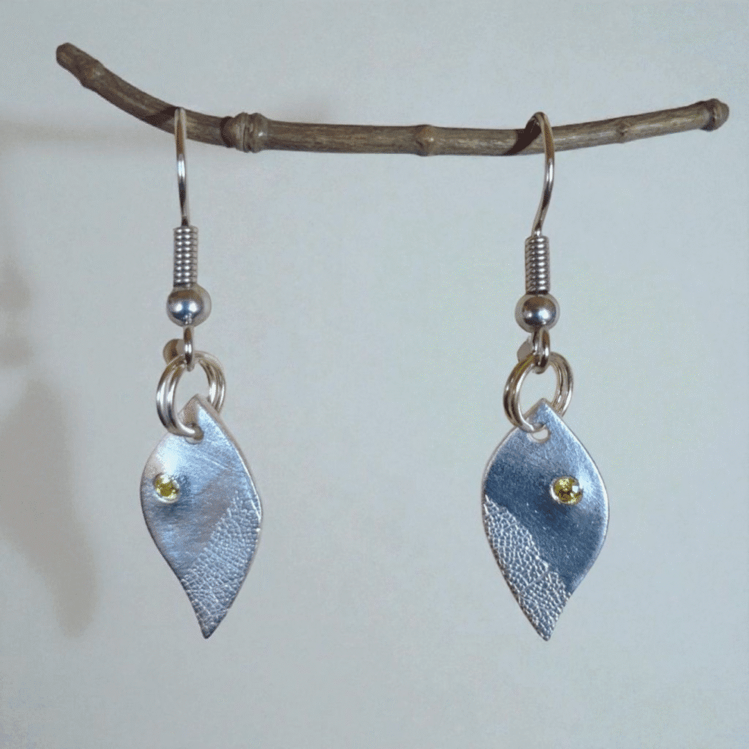 Silver leaf shaped earrings hanging from a twig. Leaf shaped earrings with skeleton leaf detail, set with cubic zirconia